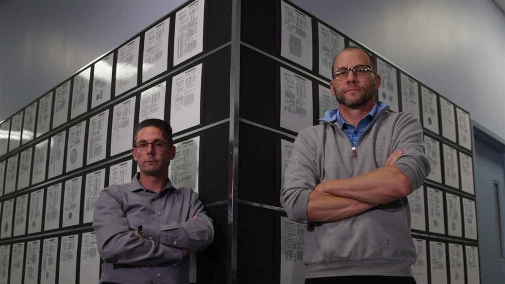 Brian Comeau and Derek Ladd stand in front of Titleist patents in Golf Ball R&D